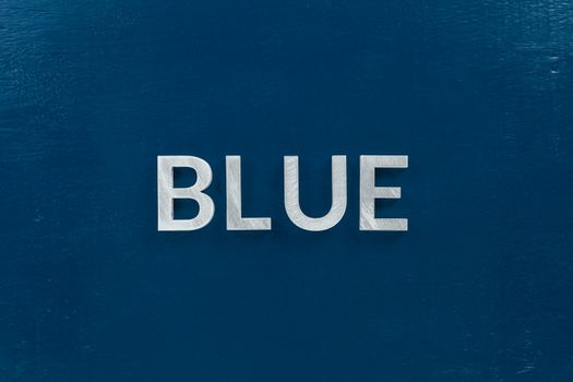 the word blue laid with silver metal letters on classic blue painted board background.