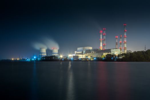 old thermal 450 megawatt power plant at night with artificial lake on foreground.