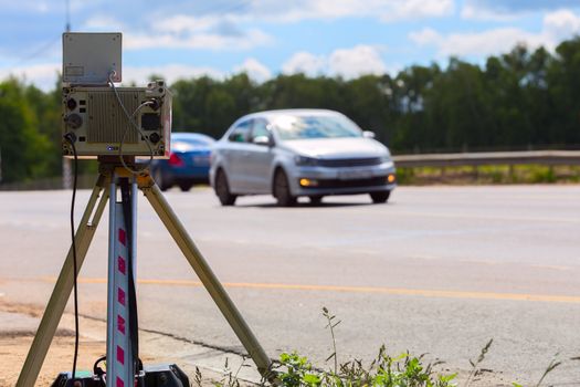 mobile speed camera device working on summer daytime road with blurry white car in background - view from back
