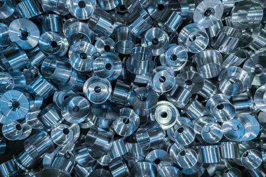 An industrial full frame background with a pile of shiny metal cnc aerospace parts. Close-up flat lay with selective focus for tech background.