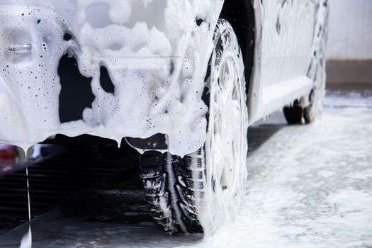 a car covered by soap foam while washing indoors - close-up low position view from back with selective focus.