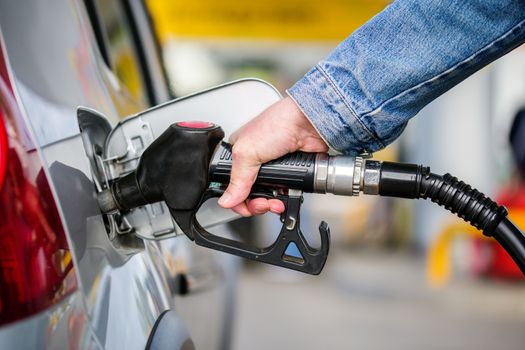 hand in jeans jacket refueling gray metallic car on gas station - closeup with selective focus and blur