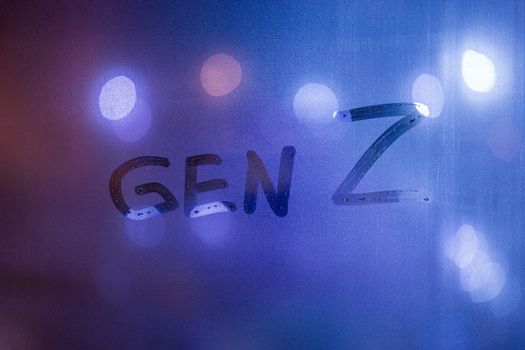 The words gen z handwritten on night wet window glass with blurry phantom blue lights in background.