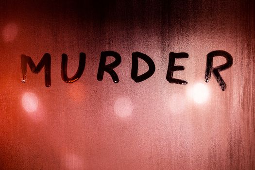 the word murder handwritten on wet glass of night window with bloody red back light of street lights.