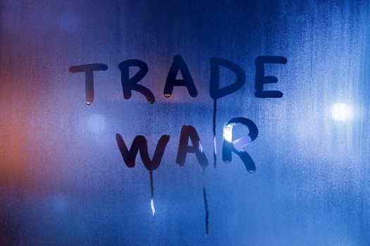 the phrase trade war handwritten on classic blue night wet window glass with selective focus and smudges