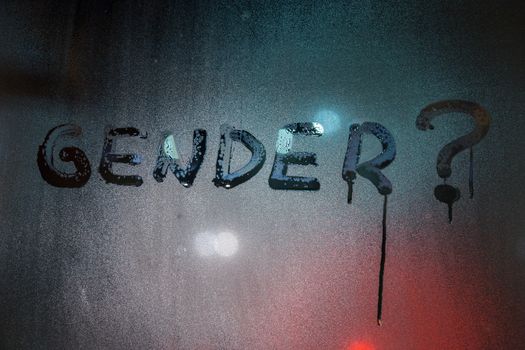the question gender written by finger on night wet glass with blurred lights in background.