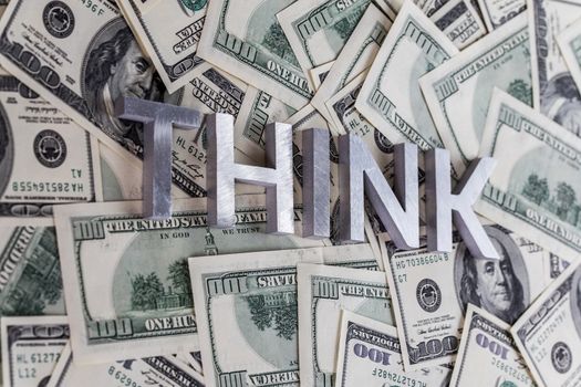 The word THINK laid with aluminium letters on the US dollar banknotes background - with selective focus and blur.