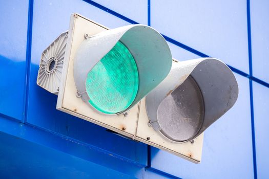 Illuminated green traffic signal light on classic blue wall of a garage.