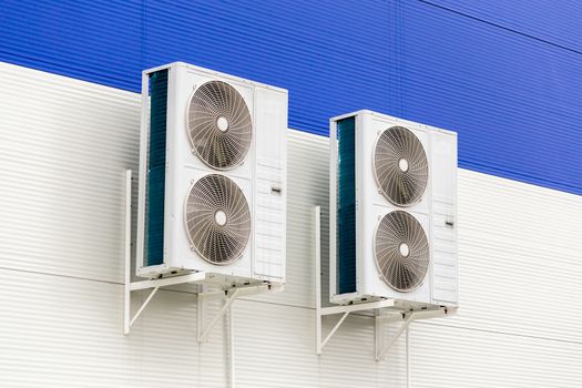 two double condensing units of air conditioner on blue and white metal industrial wall.
