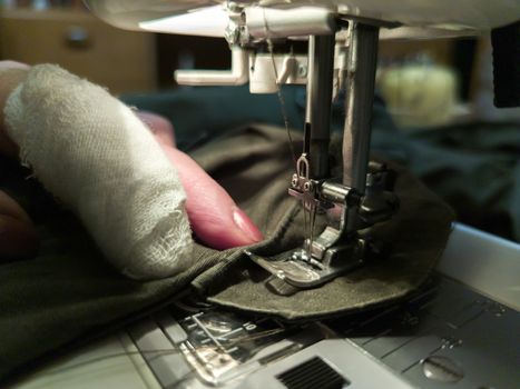 a hand of aged womans with a bandaged finger sews with a sewing machine - close-up with selective focus