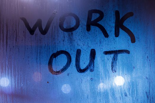 The word work out written on night sweaty window glass with blurred blue light in the background.