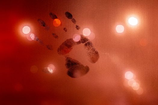 handprint on night wet glass in red colors with blurry street light in backround.