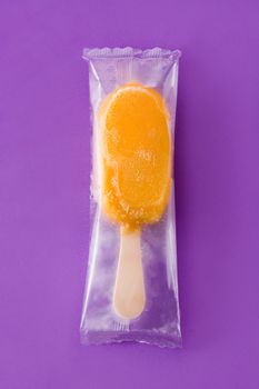 Orange popsicle packaged on violet background. Top view