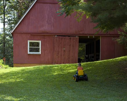 His work done for the day, a young boy drives his toy tractor toward a red barn.