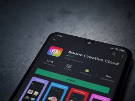 Lod, Israel - July 8, 2020: Adobe Creative Cloud app play store page on the display of a black mobile smartphone on a dark marble stone background. Top view flat lay with copy space.