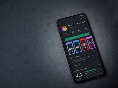 Lod, Israel - July 8, 2020: Adobe Creative Cloud app play store page on the display of a black mobile smartphone on a dark marble stone background. Top view flat lay with copy space.