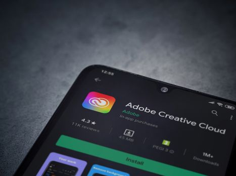 Lod, Israel - July 8, 2020: Adobe Creative Cloud app play store page on the display of a black mobile smartphone on a dark marble stone background. Top view flat lay with copy space.