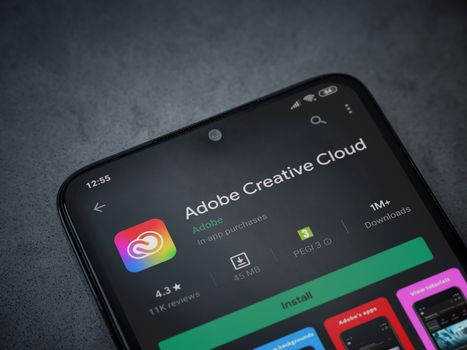 Lod, Israel - July 8, 2020: Adobe Creative Cloud app play store page on the display of a black mobile smartphone on a dark marble stone background. Top view flat lay with copy space.