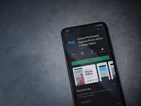 Lod, Israel - July 8, 2020: Adobe Photoshop Express Photo Editor app play store page on the display of a black mobile smartphone on a dark marble stone background. Top view flat lay with copy space.