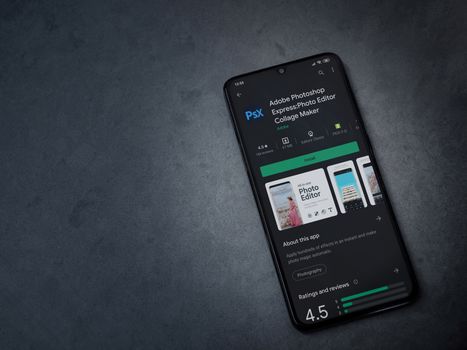 Lod, Israel - July 8, 2020: Adobe Photoshop Express Photo Editor app play store page on the display of a black mobile smartphone on a dark marble stone background. Top view flat lay with copy space.
