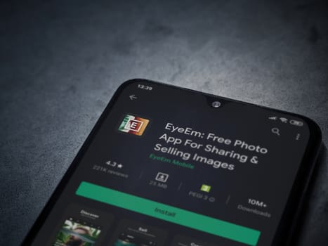 Lod, Israel - July 8, 2020: EyeEm - Sharing and Selling Images app play store page on the display of a black mobile smartphone on a dark marble stone background. Top view flat lay with copy space.