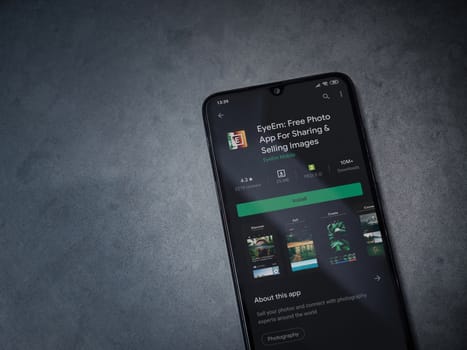 Lod, Israel - July 8, 2020: EyeEm - Sharing and Selling Images app play store page on the display of a black mobile smartphone on a dark marble stone background. Top view flat lay with copy space.