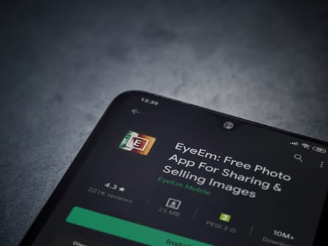 Lod, Israel - July 8, 2020: EyeEm - Sharing and Selling Images app play store page on the display of a black mobile smartphone on a dark marble stone background. Top view flat lay with copy space.