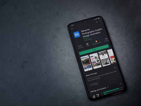 Lod, Israel - July 8, 2020: Adobe Behance app play store page on the display of a black mobile smartphone on a dark marble stone background. Top view flat lay with copy space. 
