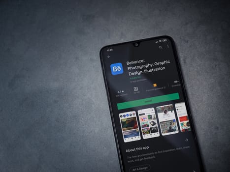 Lod, Israel - July 8, 2020: Adobe Behance app play store page on the display of a black mobile smartphone on a dark marble stone background. Top view flat lay with copy space. 