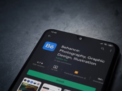 Lod, Israel - July 8, 2020: Adobe Behance app play store page on the display of a black mobile smartphone on a dark marble stone background. Top view flat lay with copy space. 
