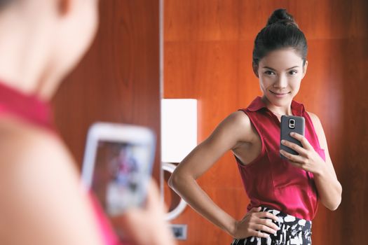 Mirror selfie confident Asian woman feeling pretty good in her body self-esteem taking photo with mobile phone in home closet looking at her slim weight loss waistline.