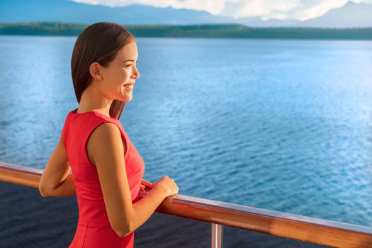Luxury travel cruise ship elegant Asian woman on Alaska destination cruising holiday. Happy lady looking at sunset view of ocean from boat balcony deck.