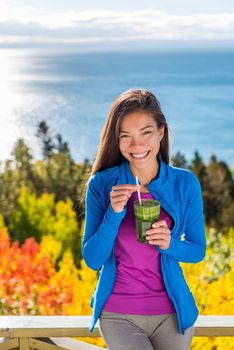 Healthy food living clean eating woman drinking fresh spinach vegetable smoothie in beautiful outdoors autumn nature at resort travel lodge with ocean view. Happy asian girl fitness life.
