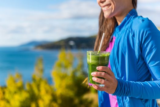Healthy diet health conscious woman happy smiling drinking fresh green vegetable smoothie as a detox morning breakfast in beautiful autumn sun nature outdoors. View of ocean and mountains.