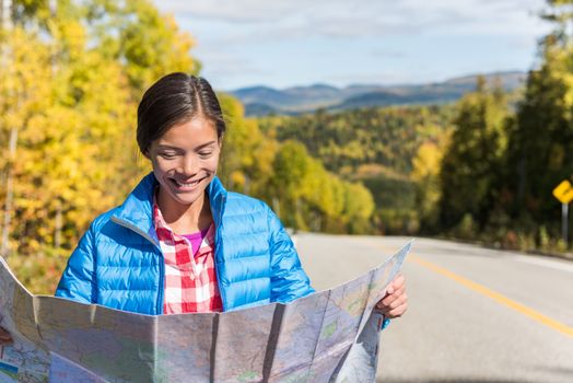 asian hiker woman on adventure nature travel looking at map directions against autumn landscape during road trip. Happy tourist searching her way on car driving holidays in forest outdoors.