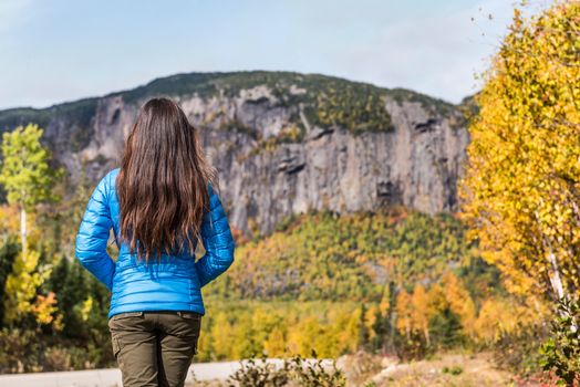 Nature outdoors travel woman mountain lifestyle, unrecognizable brunette hiking girl wearing blue down jacket relaxing looking at view of fall season scenic landscape at park during camping trip.