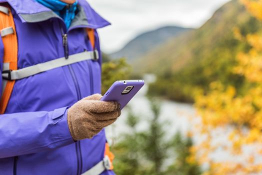 Person hiking in nature using smartphone app with touch screen tech gloves during hike in autumn travel adventure in mountain forest outdoors. Beautiful landscape background.
