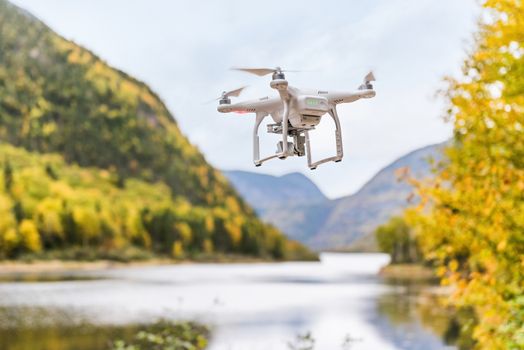 Drone uav flying in the air taking video of autumn forest foliage nature landscape in outdoors during fall season. Quad copter with digital camera hovering in sky over beautiful lake.