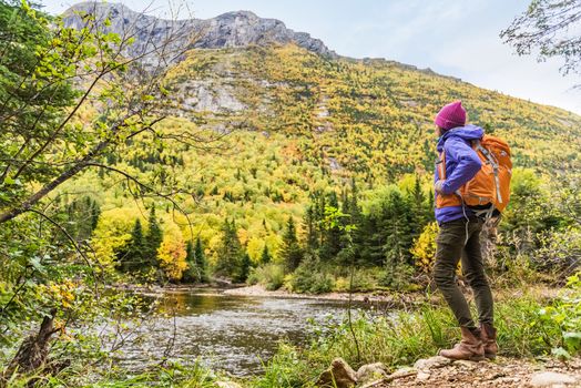 Woman hiker hiking looking at scenic view of fall foliage mountain landscape . Adventure travel outdoors person standing relaxing near river during nature hike in autumn season.