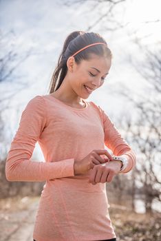 Woman preparing fitness smart watch for running. Sportswoman getting ready for morning run in cold fresh air outdoor nature checking watch device setting for cardio workout.