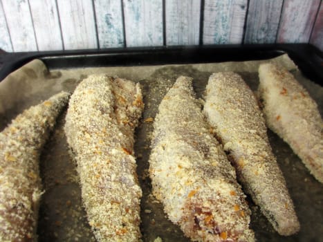 fresh sea fish breaded in breadcrumbs and prepared for baking on a baking sheet