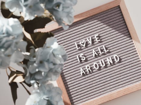 Top view on letter board with words LOVE IS ALL AROUND. Flat lay concept heart symbol of love and romance. Blue hydrangea flowers.