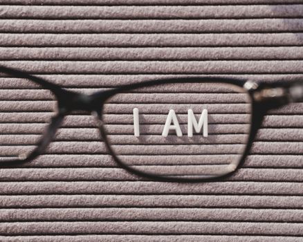 Top view on letterboard with words I AM through eyeglasses. Flat lay concept of psychological self-regulation or gender identity. Social psychological issue. Closer look on psychological problems.