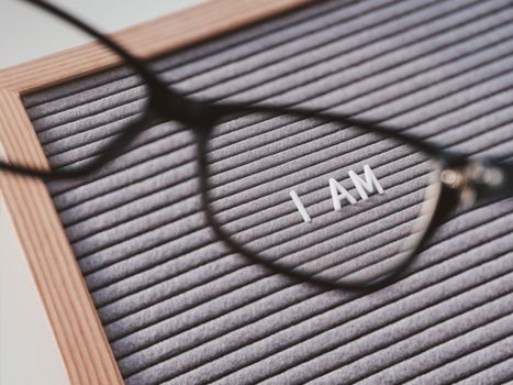Top view on letterboard with words I AM through eyeglasses. Flat lay concept of psychological self-regulation or gender gender identity. Social psycological issue. Closer look on psychological problems.
