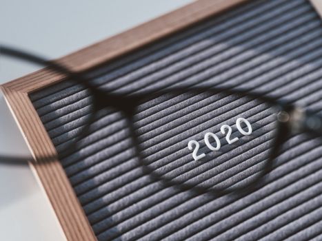 Top view on letterboard with numbers 2020 through eyeglasses. Flat lay concept of 2020 year results. 2020 review. Social, political or economical issue. Closer look on problems and achievements.