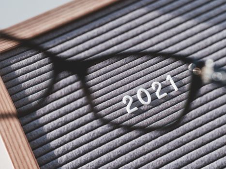 Top view on letterboard with numbers 2021 through eyeglasses. Flat lay concept of 2021 year results. 2021 review. Social, political or economical issue. Closer look on problems and achievements.