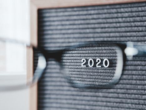 Top view on letterboard with numbers 2020 through eyeglasses. Flat lay concept of 2020 year results. 2020 review. Social, political or economical issue. Closer look on problems and achievements.