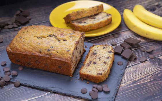 Banana bread on cutting board with chocolate chips and fresh banana in background.