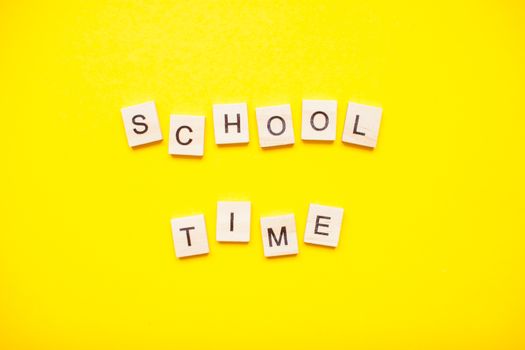 Words from wooden blocks "school time" on bright yellow background