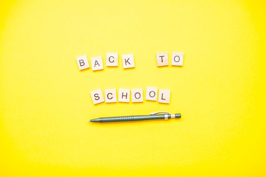 Words from wooden blocks "back to school" and stationery on bright yellow background